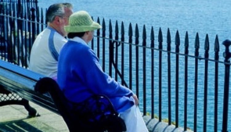 An elderly couple sitting outside on a bench 