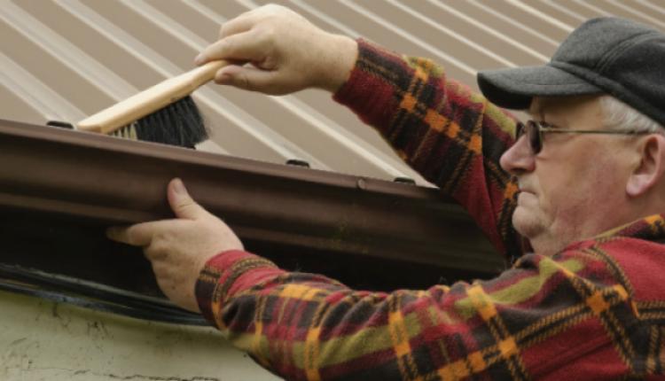 An elderly man cleaning the house gutters 