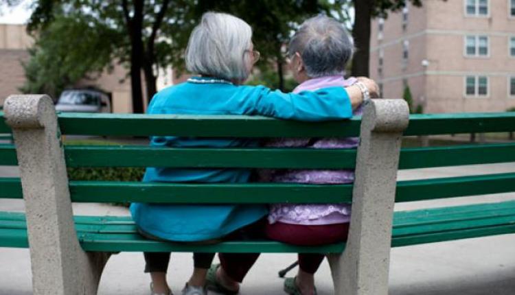 兩位老年女性坐在公園的長椅上。一個女性的手臂放在另一個女性的肩膀上。