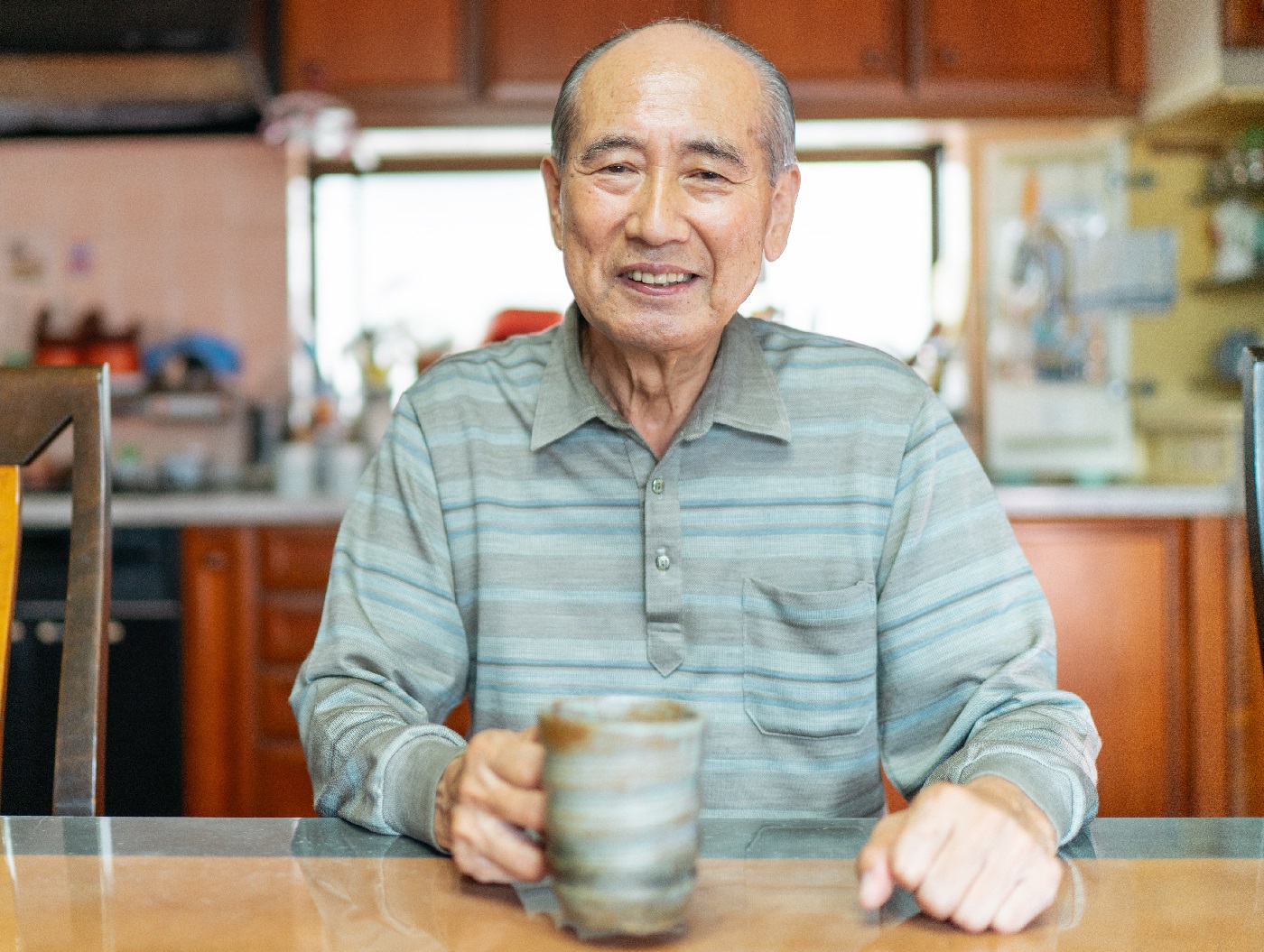 Portrait of happy senior man at home in the kitchen, holding a coffee mug