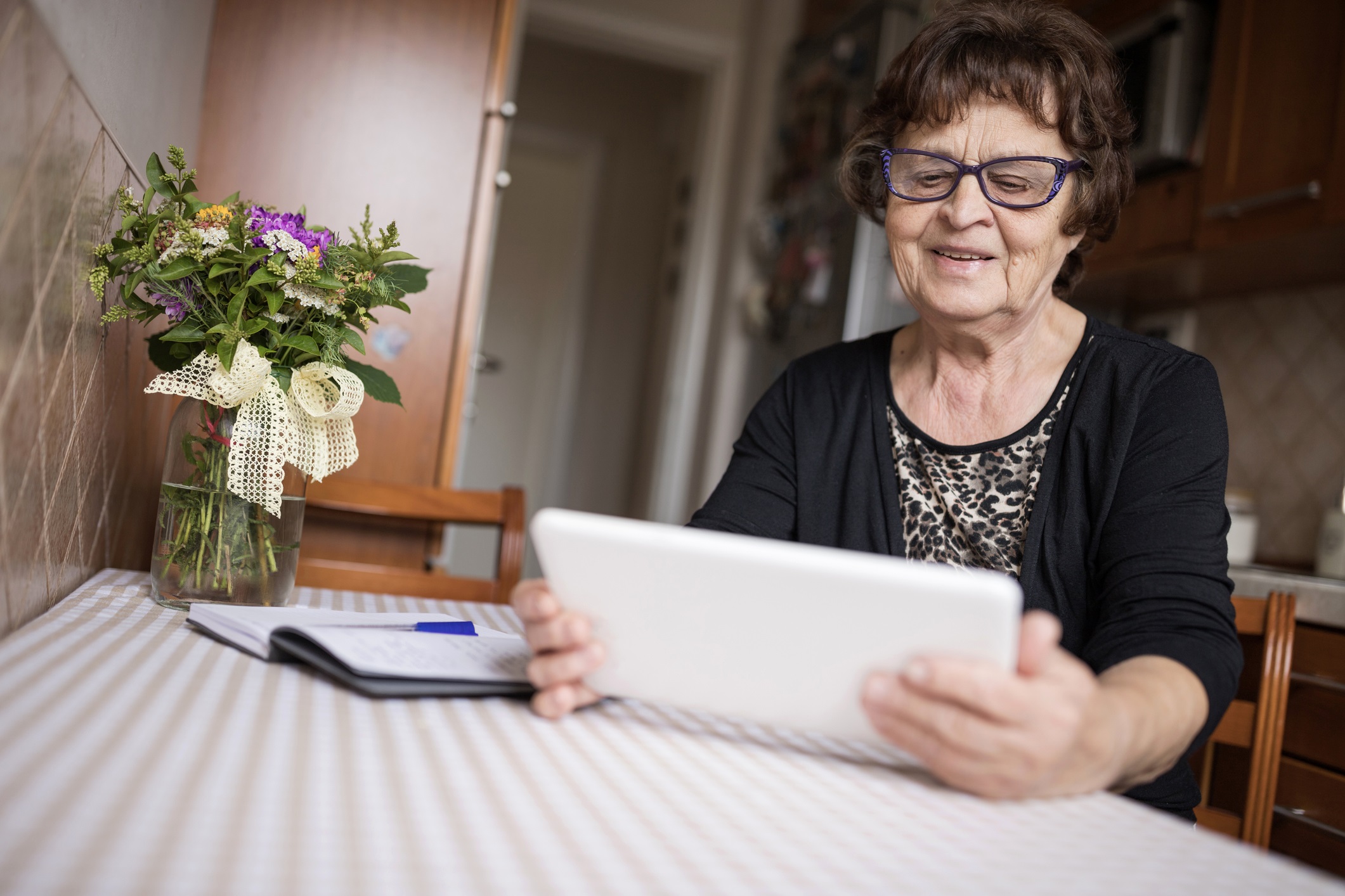 Senior woman with eyeglasses sitting at a table and using digital tablet at home